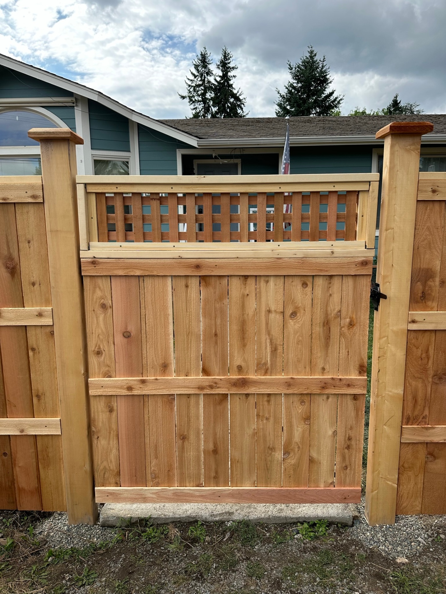 Cedar walk gate with vertical boards, horizontal cap rail, and a square-lattice topper matching the adjacent privacy fence